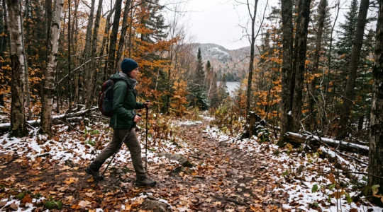 Un randonneur marche sur un sentier forestier canadien où les feuilles d'automne côtoient les premières neiges de la saison.